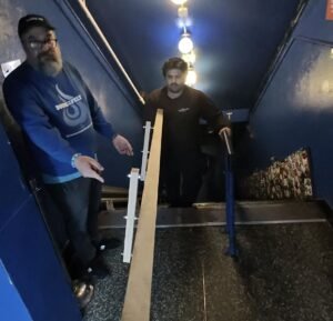 Commercial shuffleboard movers carrying a table section down a tight staircase